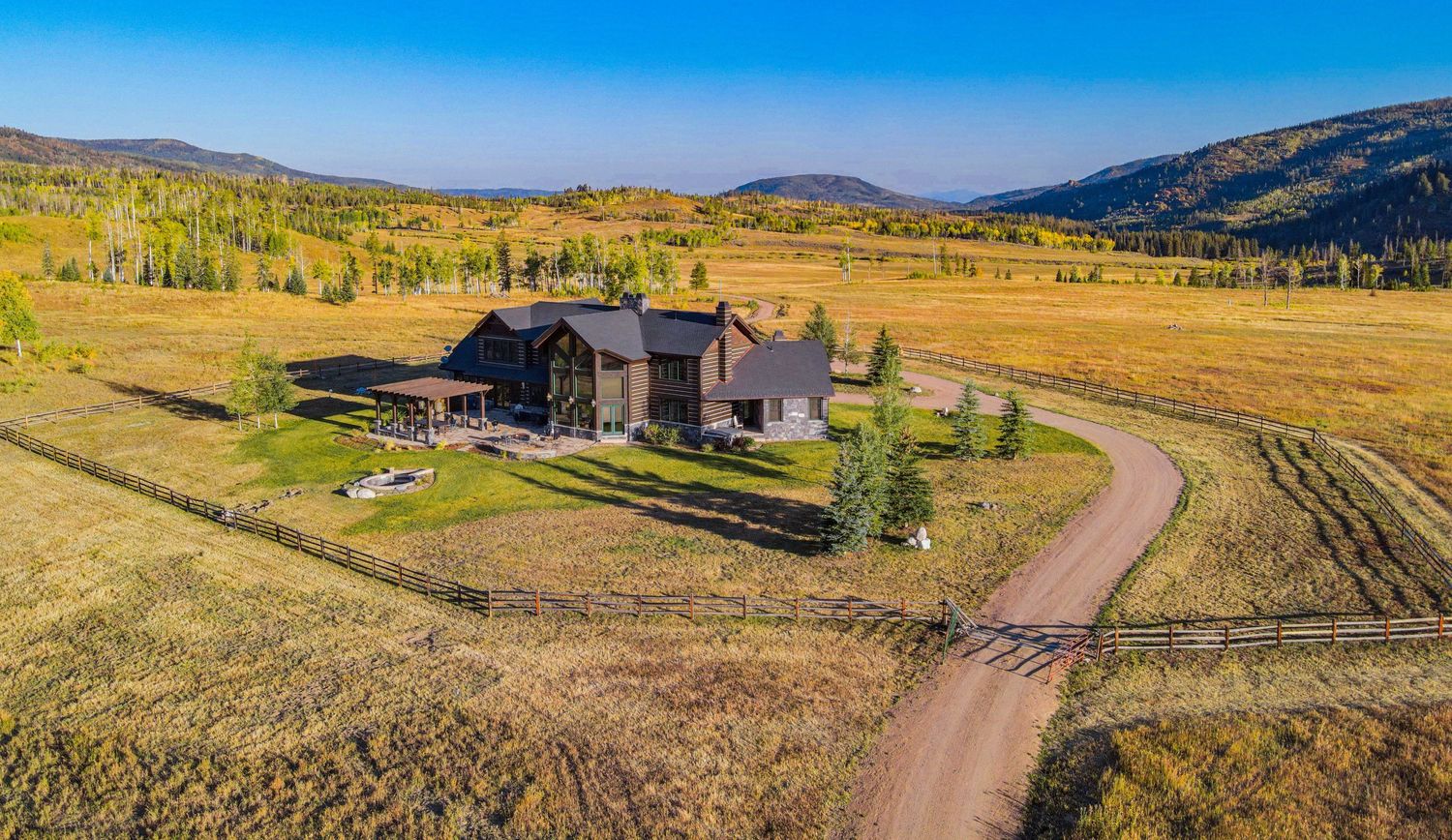Aerial view of a luxury Colorado ranch home surrounded by vast meadows and colorful autumn foliage in a mountain valley.