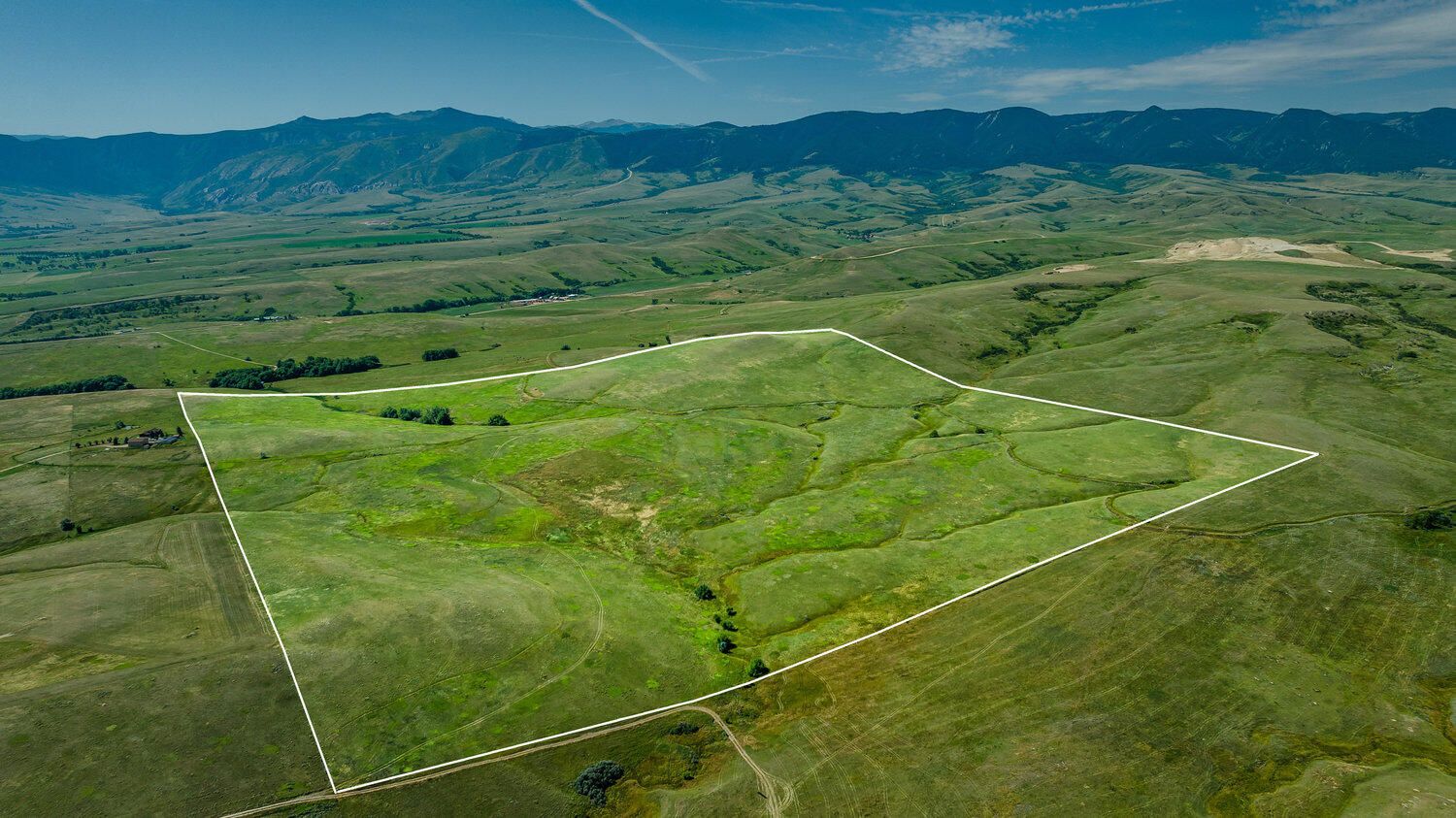 Aerial view of lush green rolling hills and mountain landscape with outlined property boundary in rural countryside.
