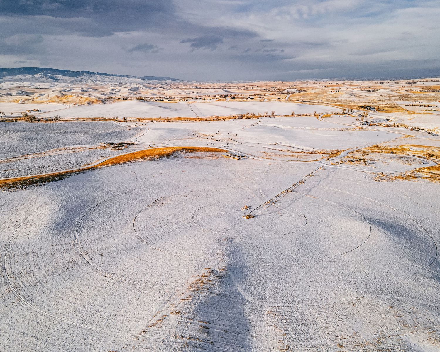 Aerial view of snow-covered rolling hills with patches of exposed ground creating a winter landscape pattern.