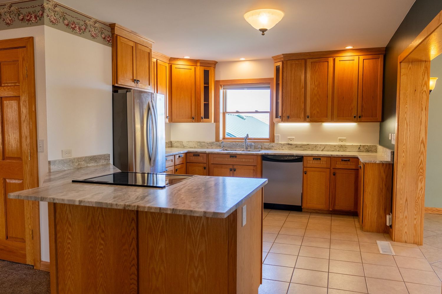 Spacious kitchen with oak cabinets, granite island, stainless steel appliances, and light tile flooring.
