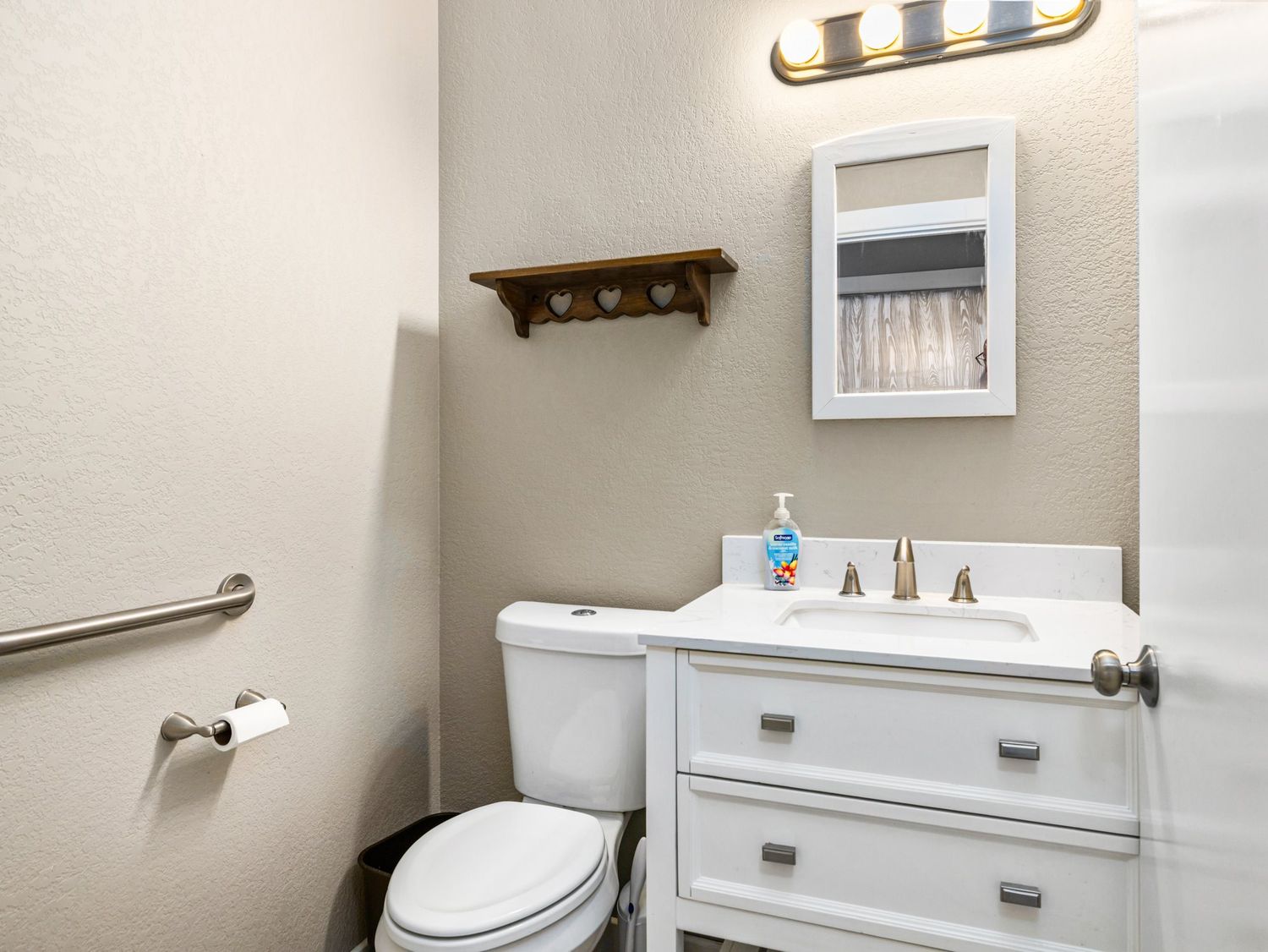Small bathroom with white vanity, toilet, medicine cabinet mirror, and decorative shelf above.