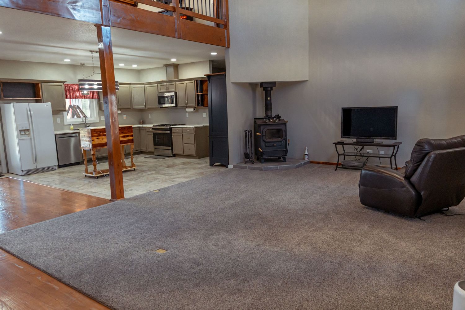 Open concept living space with kitchen, wood beams, and stone fireplace.