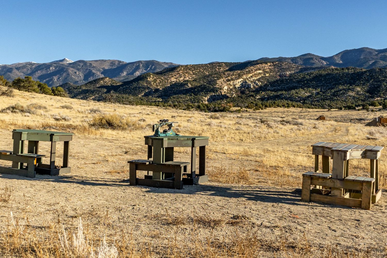 Desert shooting range with wooden target stands against mountainous backdrop.