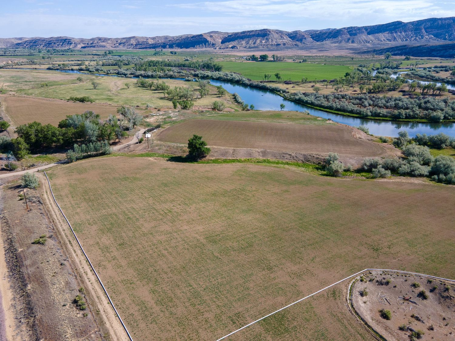 Aerial view of expansive farmland along a winding river with lush green fields and mountain backdrop.