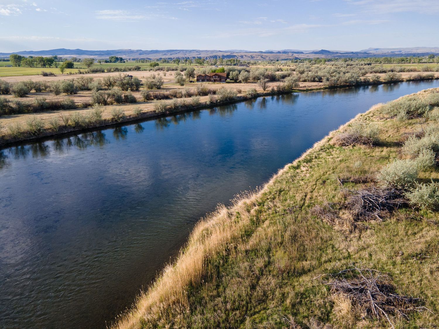 Aerial view of a winding blue river with golden marsh grasses and sagebrush along the banks under clear skies.