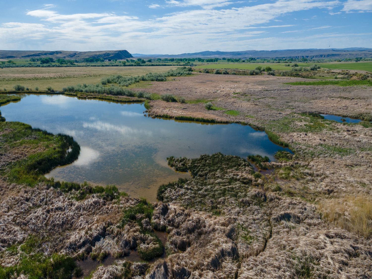 Aerial view of a heart-shaped pond surrounded by rocky terrain and shrubland in a vast rural landscape.