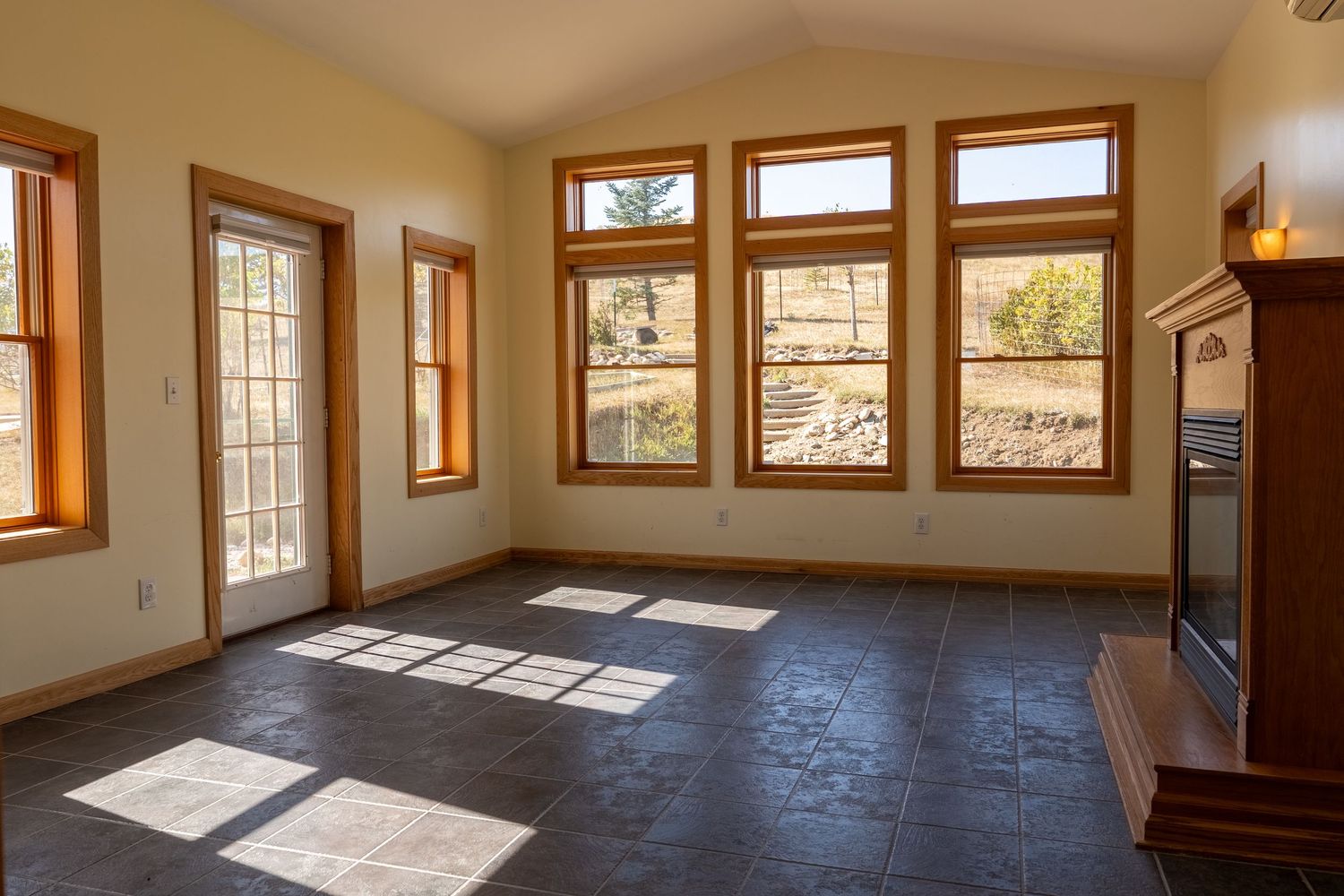Bright sunlit living room with dark tile floors, wood-trimmed windows, and a fireplace in a modern home.