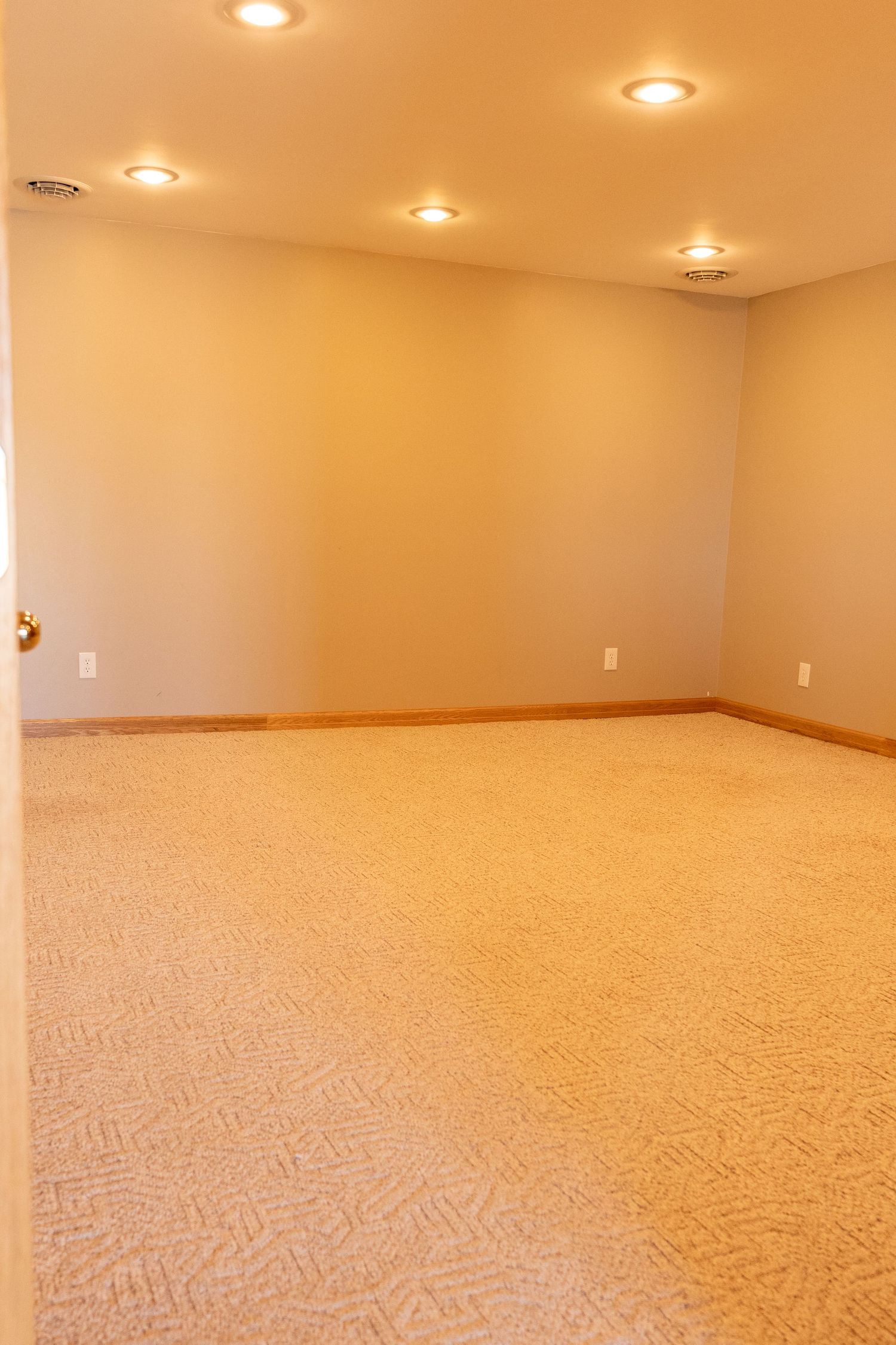 Empty carpeted room with beige walls, recessed lighting, and wood baseboards in a clean, move-in ready space.