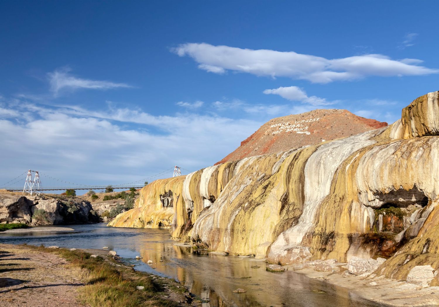 Colorful mineral terraces and hot springs under a blue sky with white clouds in a desert landscape.