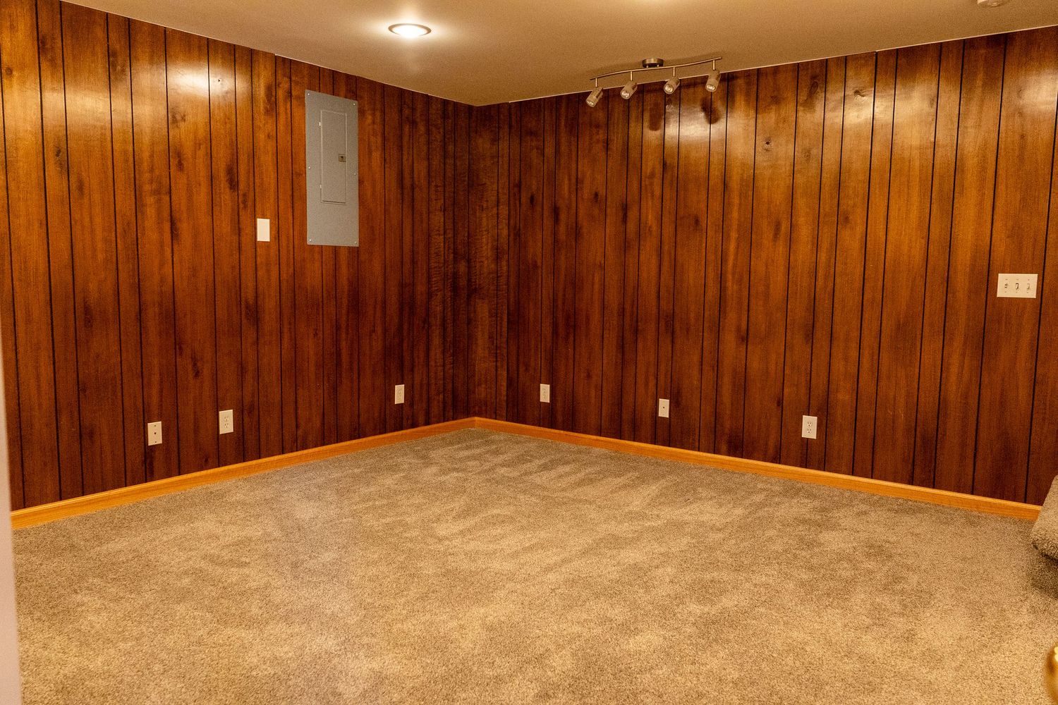 Empty room with wood-paneled walls, beige carpet, and recessed lighting in a finished basement.