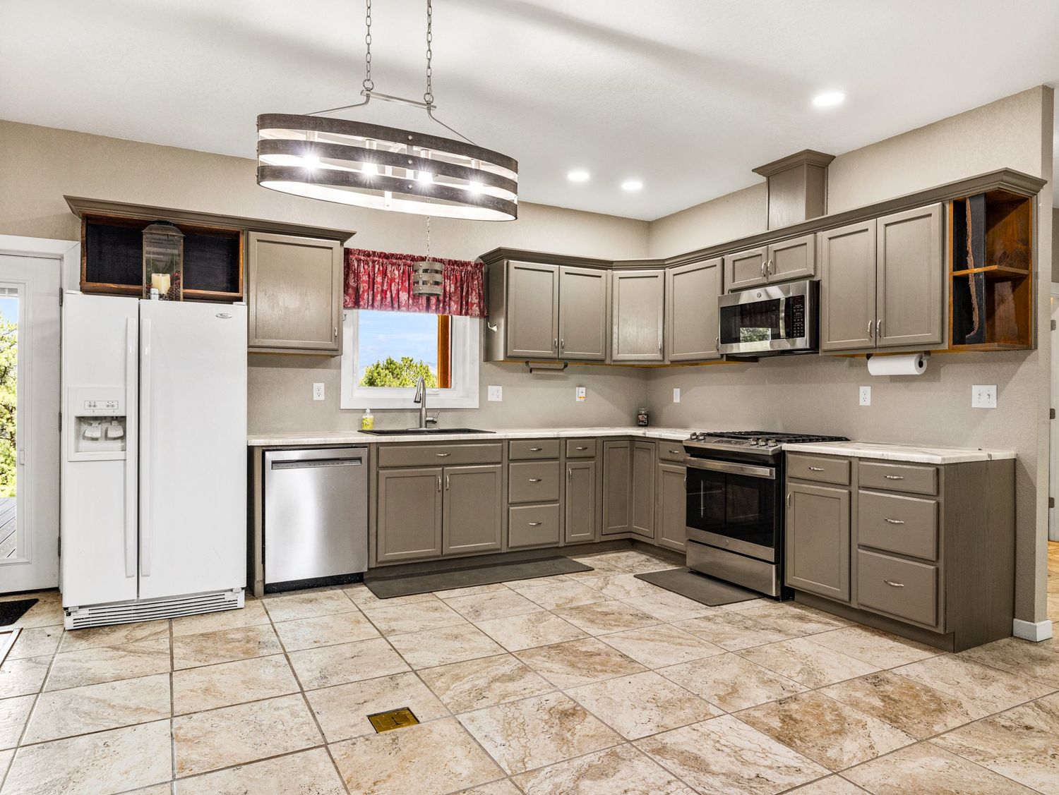 Spacious kitchen with gray cabinets, stainless steel appliances, white refrigerator, and tile flooring with pendant lighting.