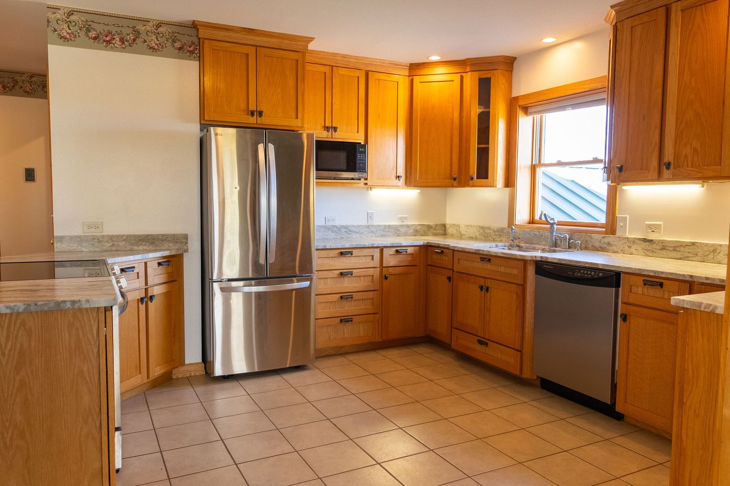 Modern kitchen with oak cabinets, granite countertops, stainless steel appliances, and tile flooring in a bright, well-lit space.