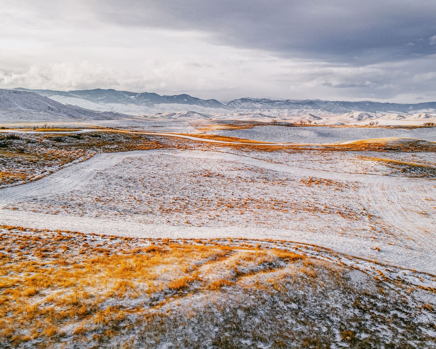 Snow-covered hills with orange-tinted vegetation and mountain ranges in the distance.