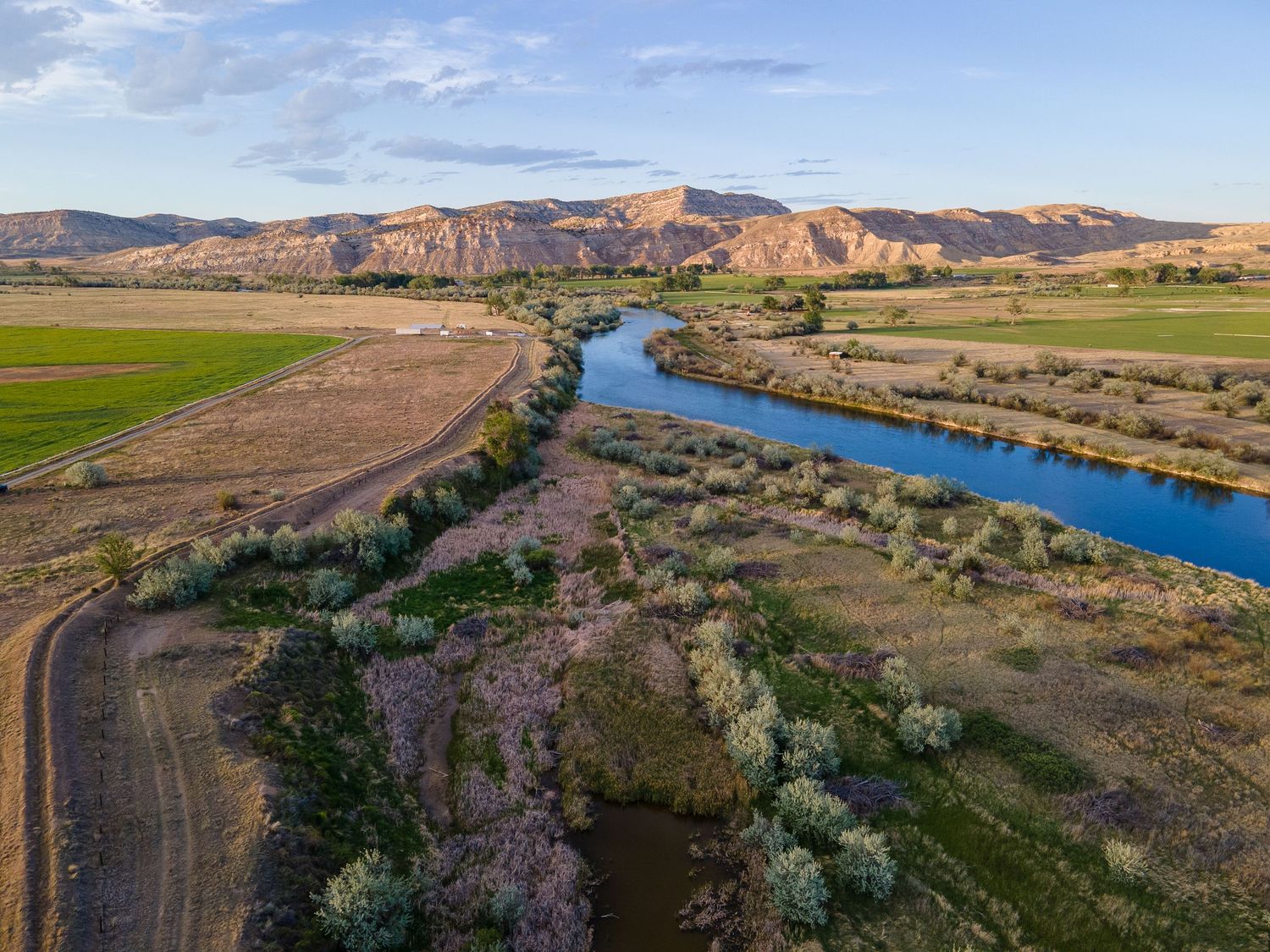 Aerial view of a blue river flowing through a scenic valley with mountains and farmland.