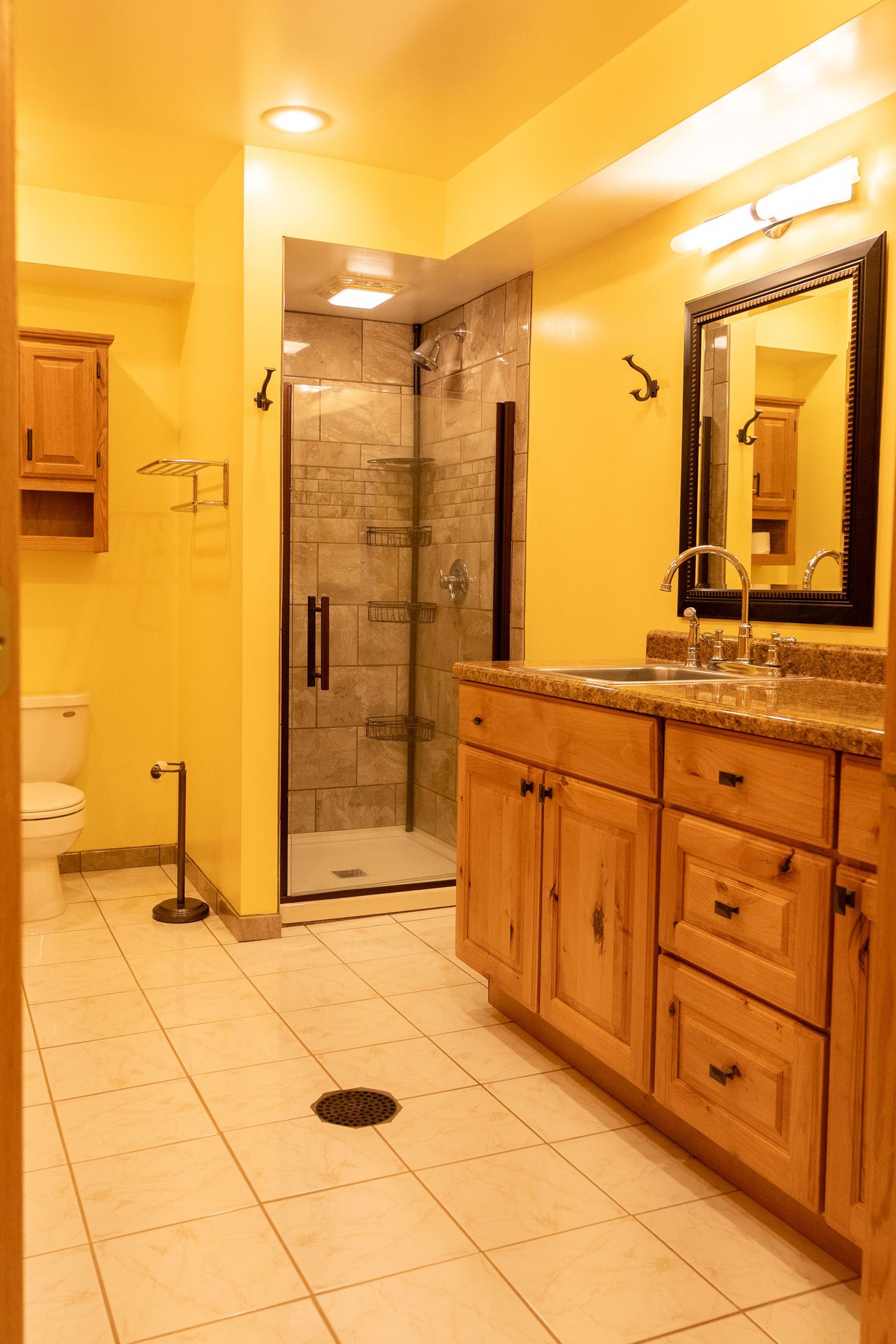 Spacious bathroom with wooden vanity, granite countertop, walk-in tile shower, large mirror, and white tile floors.