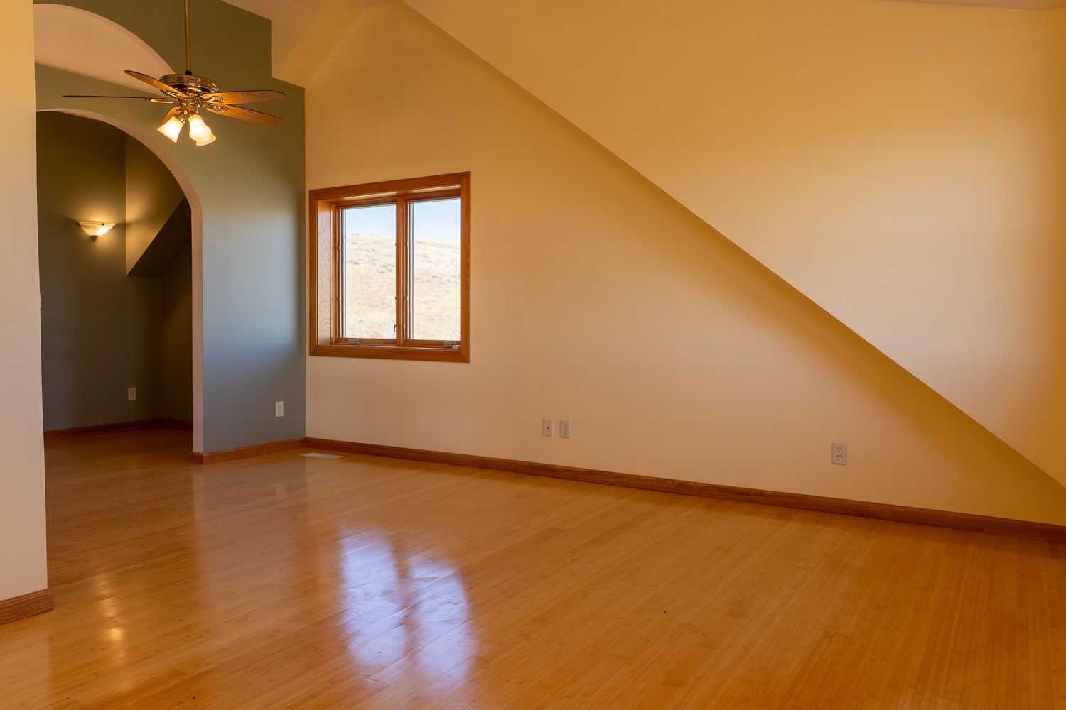 Empty room with hardwood floors, vaulted ceiling, ceiling fan, arched doorway, and a window with natural light.