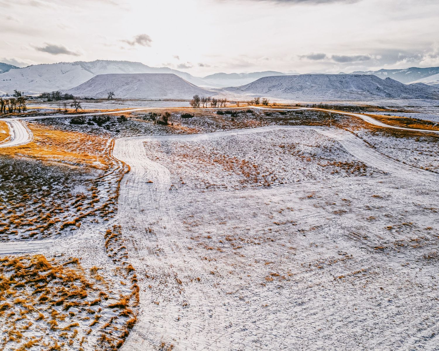 Snow-covered winter landscape with winding roads through rolling hills.