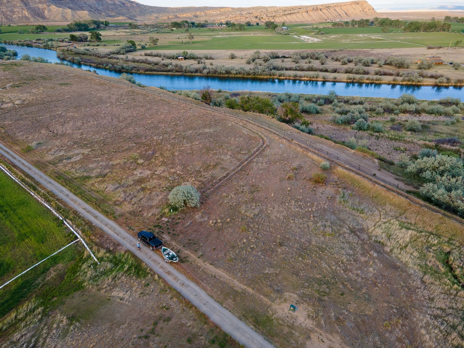 Aerial view of a rural road along a river with arid fields and rocky bluffs.