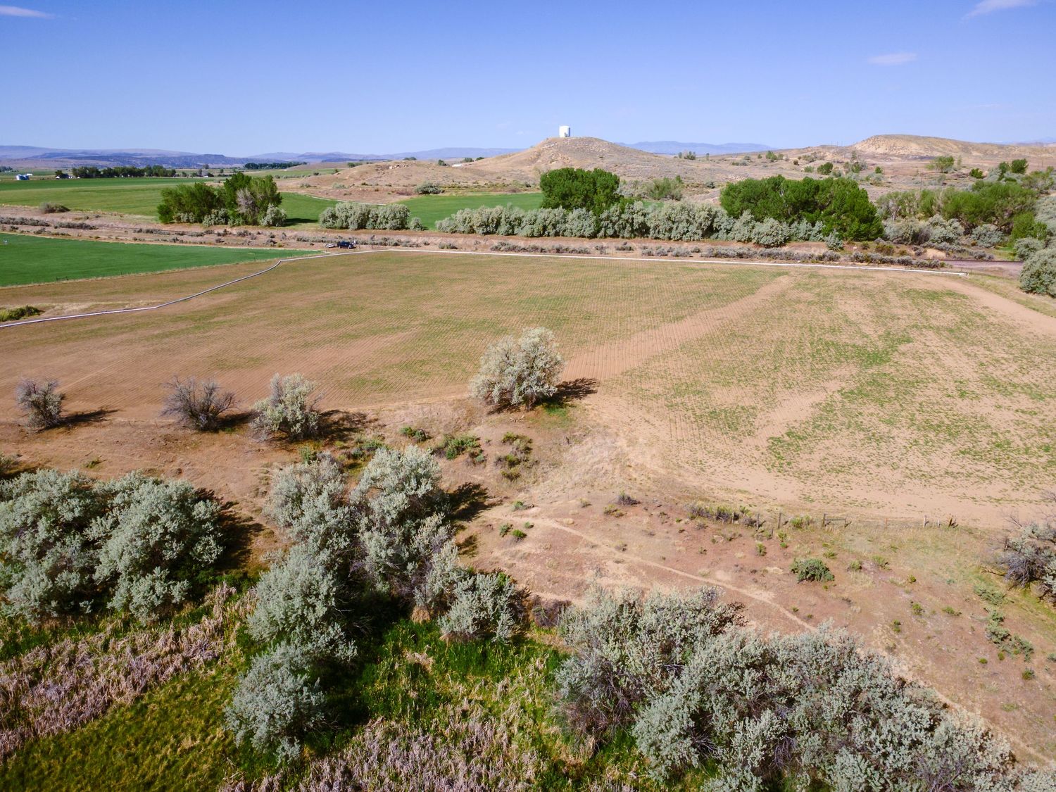 Aerial view of sparse sagebrush, dry open land, and lush green irrigated fields with hills in the background.