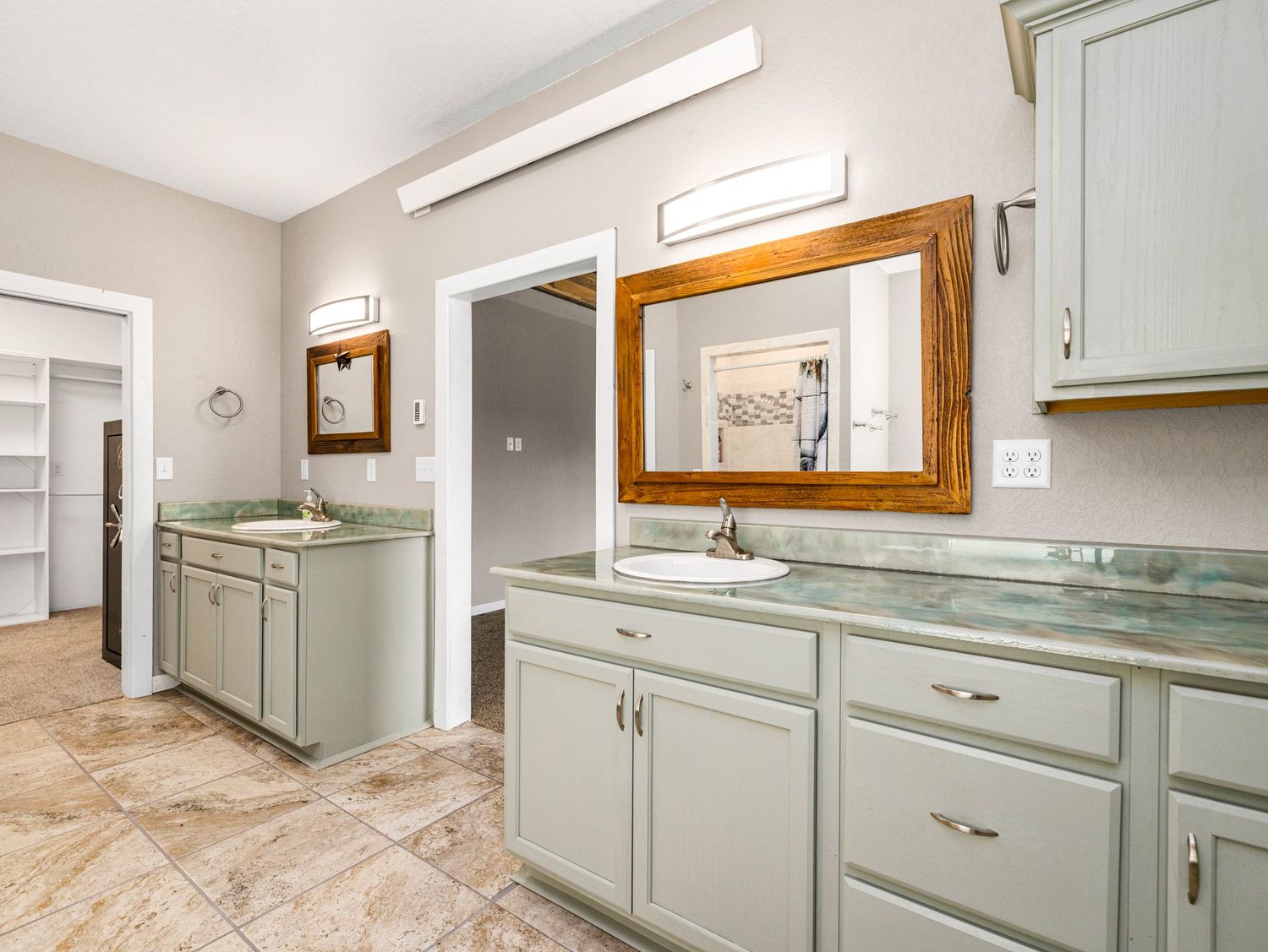 Spacious bathroom with dual sinks, sage green cabinets, green granite countertops, and a wood-framed mirror.