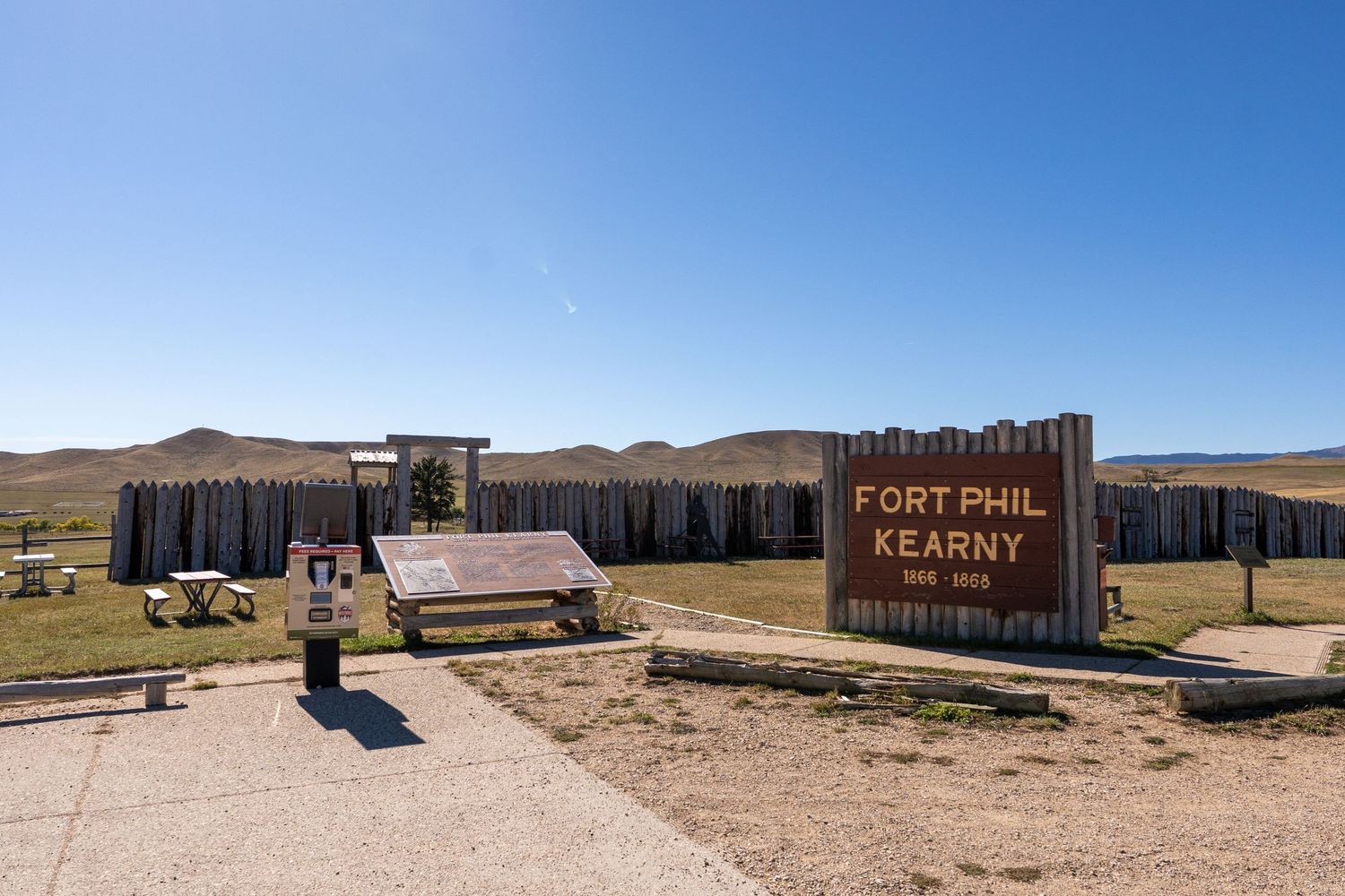 Historic Fort Phil Kearny site with wooden stockade walls and entrance sign under clear blue sky in Wyoming.