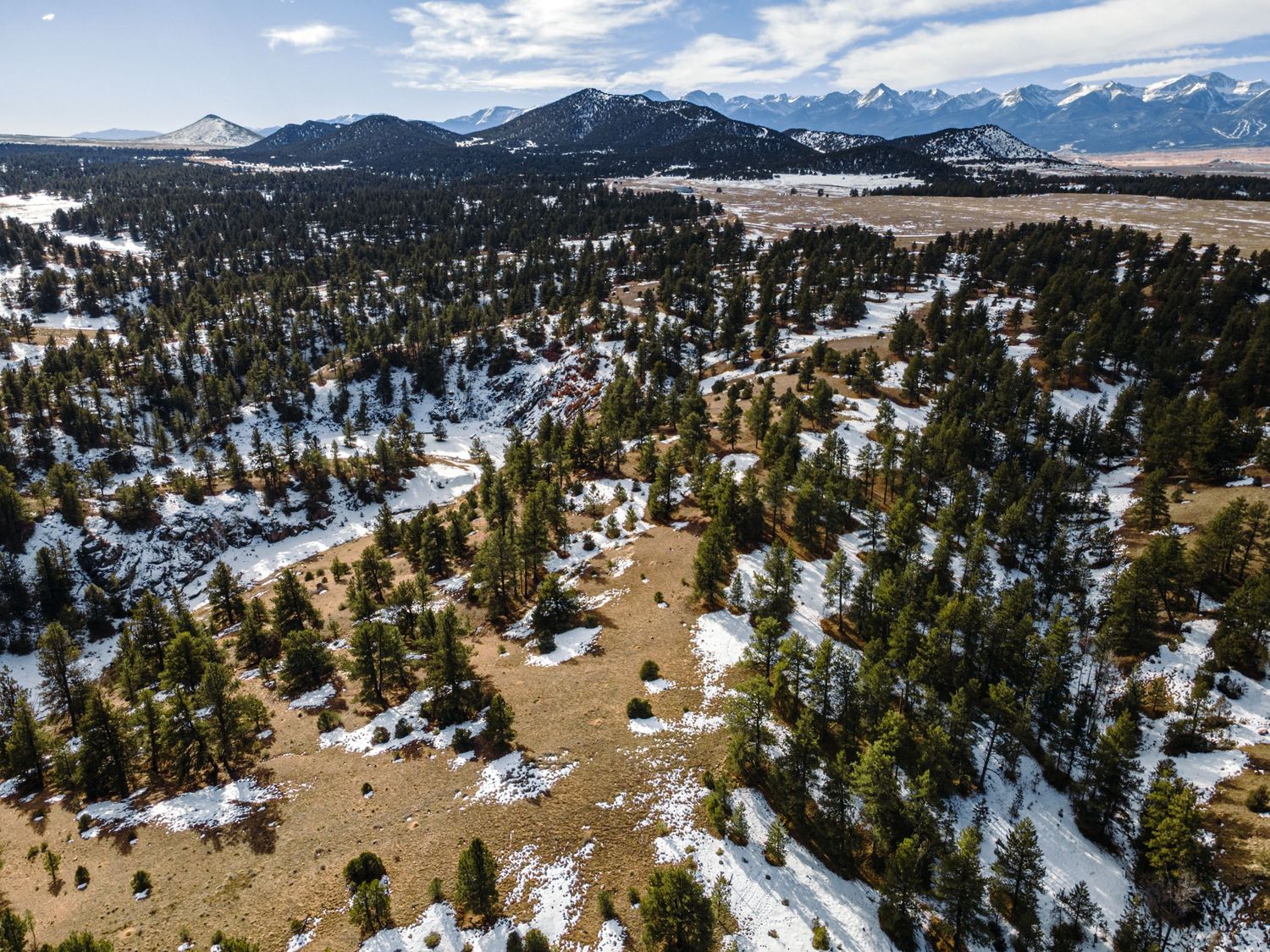 Winter aerial view of mountain landscape with snow-covered forest and scattered clearings.