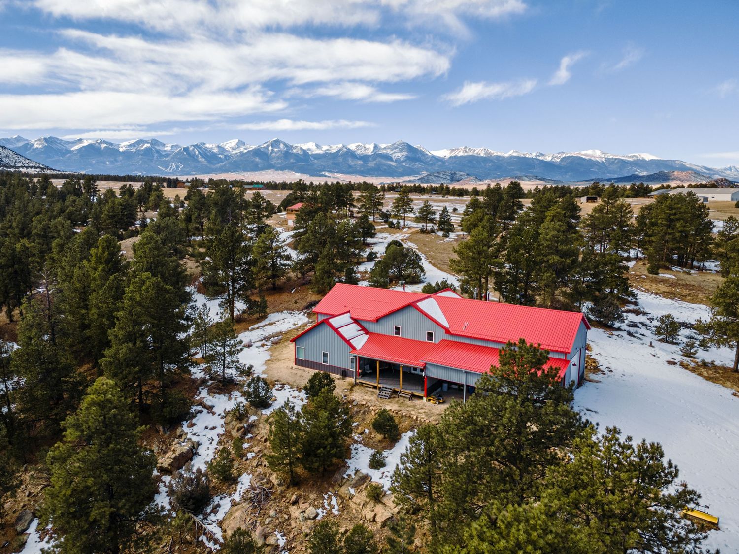 Snow-covered mountain property featuring red-roofed structures amid evergreen forest with mountain views.