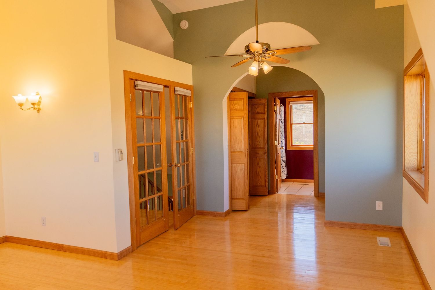 Bright open entryway with hardwood floors, arched hallway, ceiling fan, French doors, and high vaulted ceilings in a modern home.