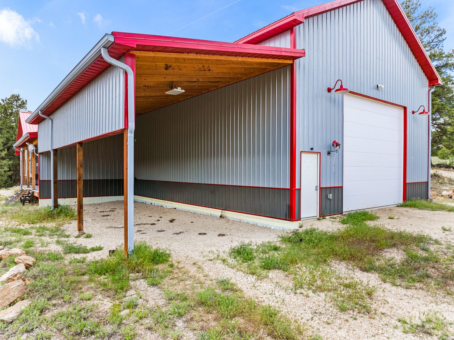 Large metal pole barn with red trim, open bay, and white garage door on a gravel lot.