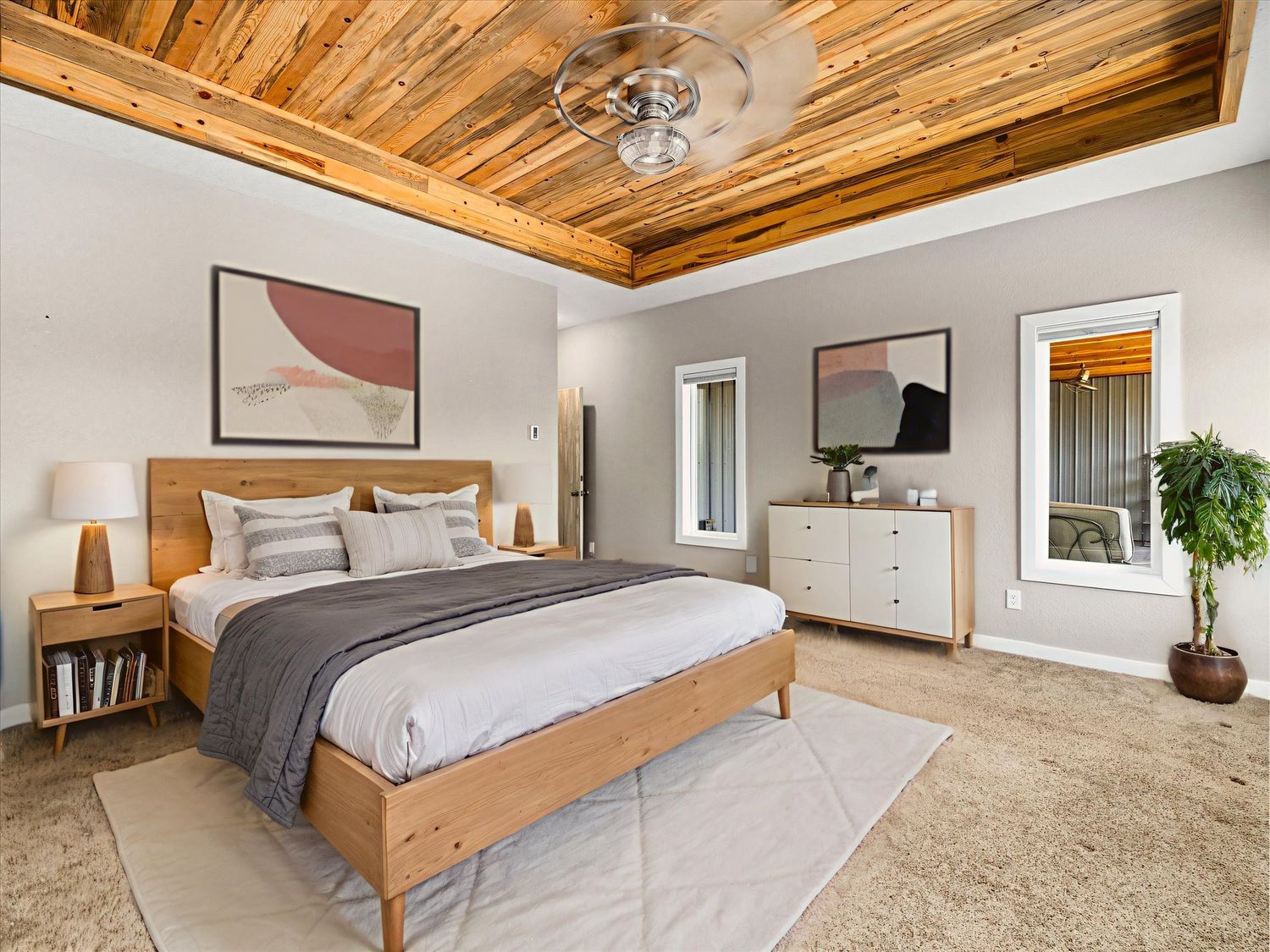 Spacious primary bedroom with wood plank tray ceiling, natural light, plush carpet, and modern wooden bed frame with neutral decor.