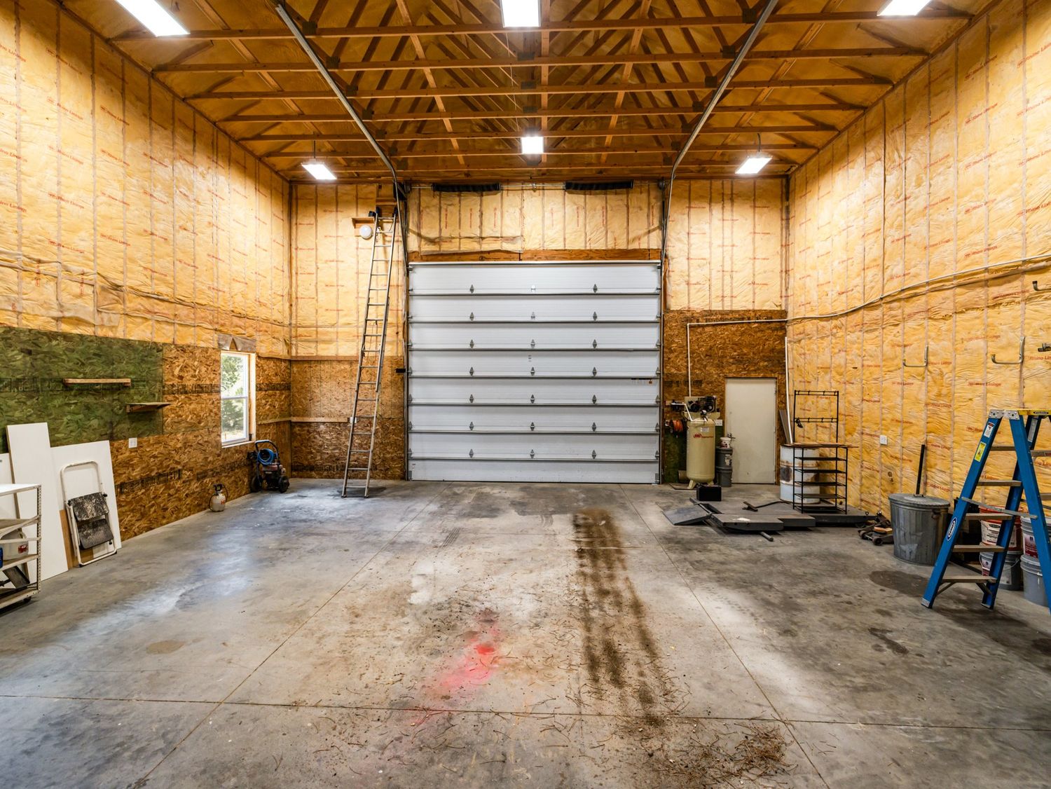 Spacious garage workshop with high ceilings, large roll-up door, and concrete floor.