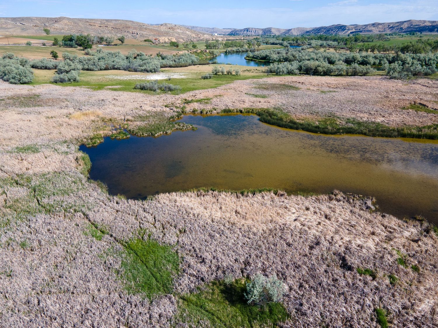 Aerial view of a serene pond surrounded by dry grassland and green shrubs in a scenic valley landscape.