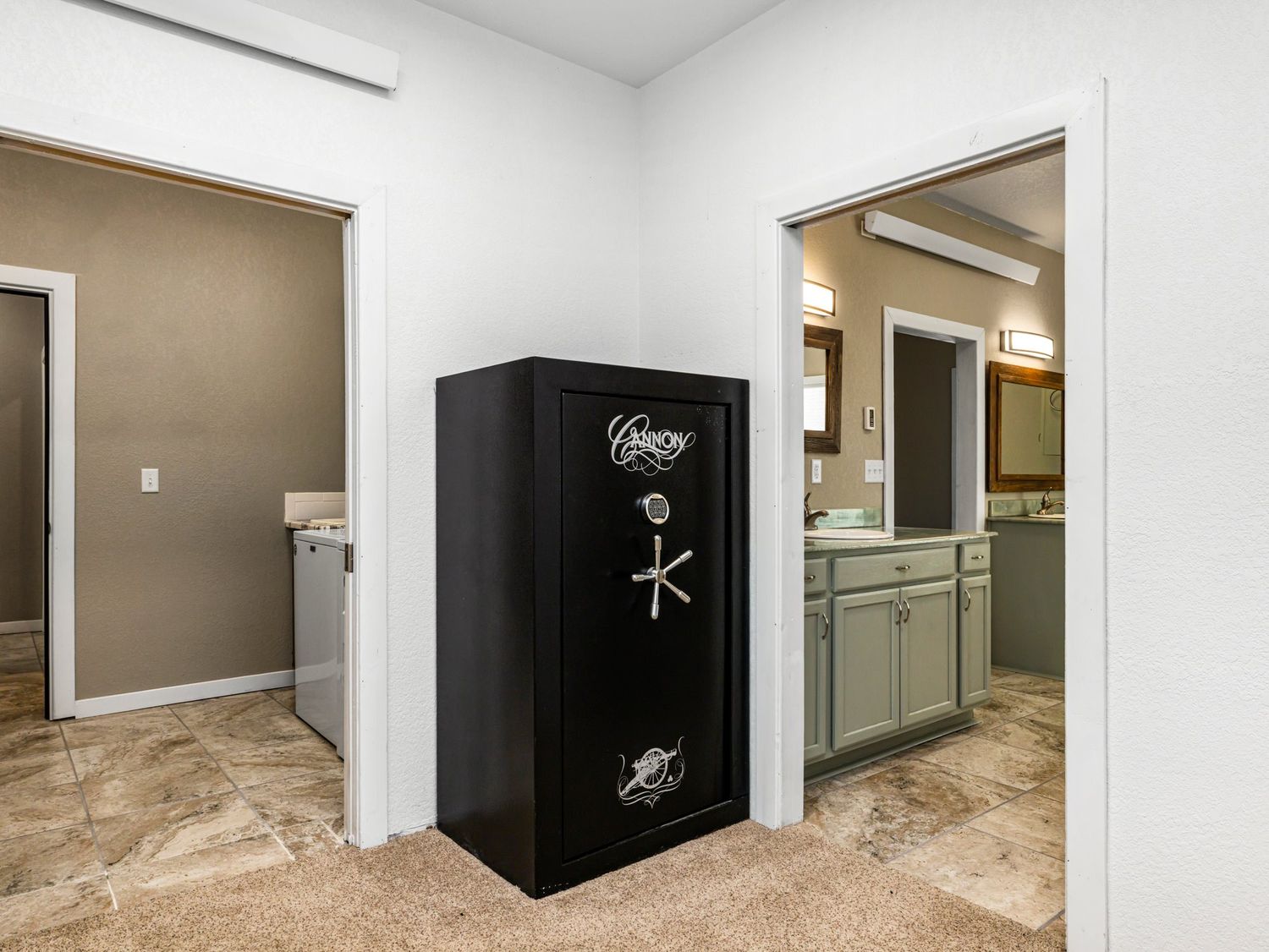 Black gun safe stands between a laundry room and bathroom with green cabinets in a home interior.
