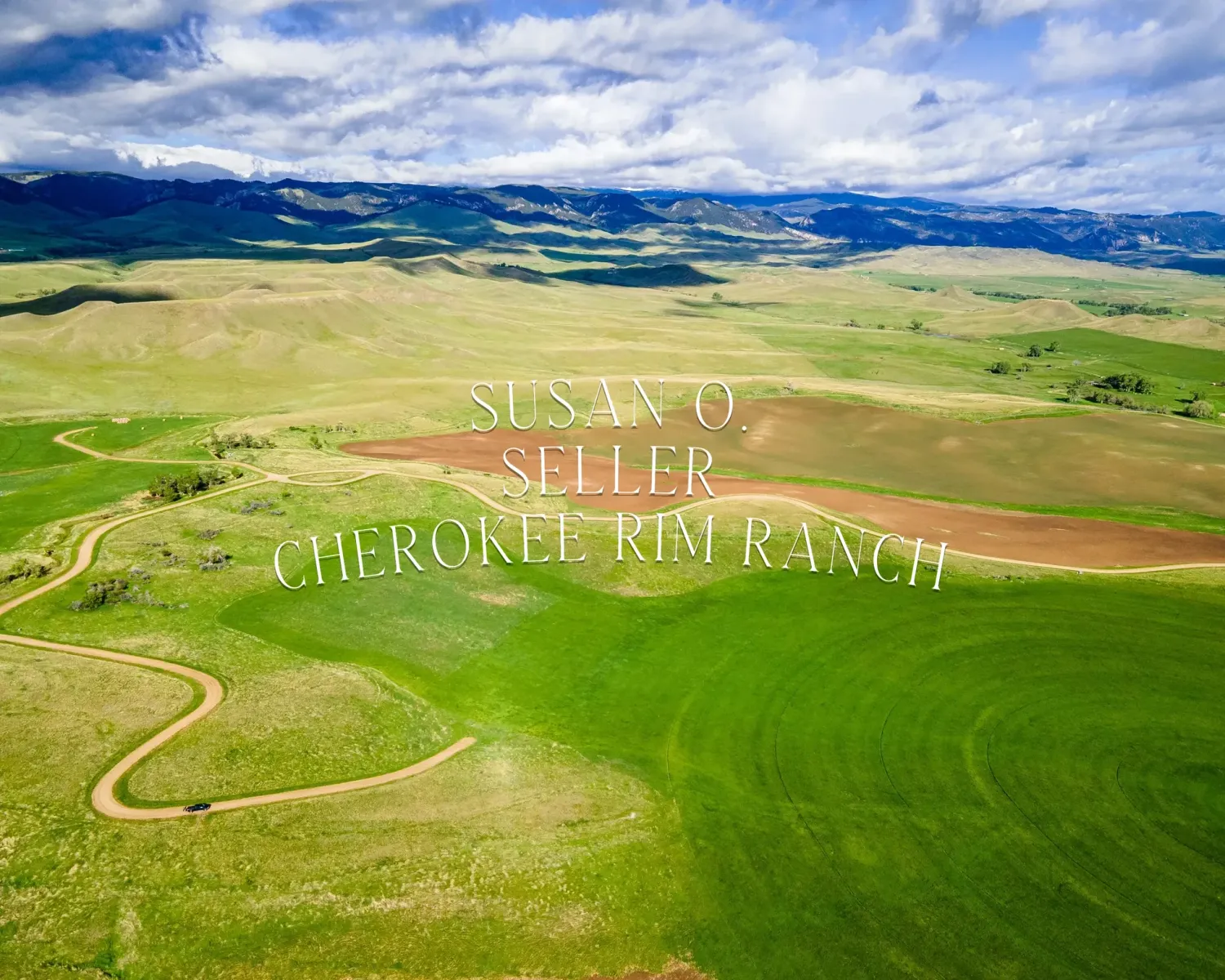 Panoramic drone shot of vast ranch land with winding dirt roads through green pastures and mountains.