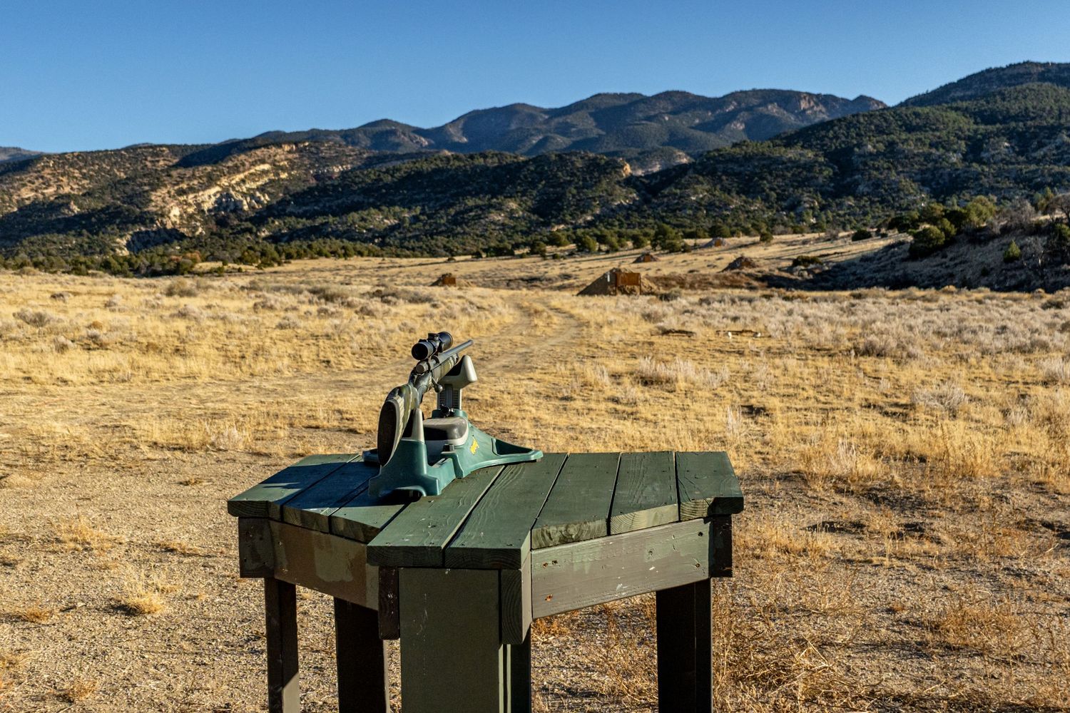 Bronze horse sculpture on a green pedestal overlooking golden grasslands and mountain range under clear blue sky.