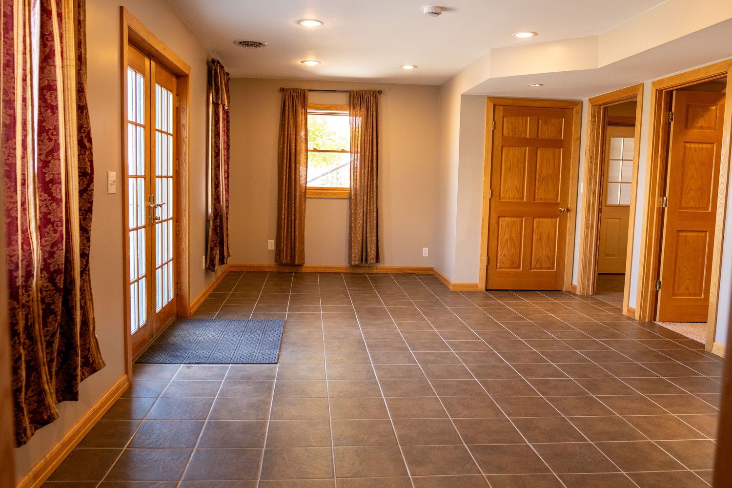 Spacious empty room with dark tile floors, wood trim, French doors, and multiple wooden interior doors in neutral tones.