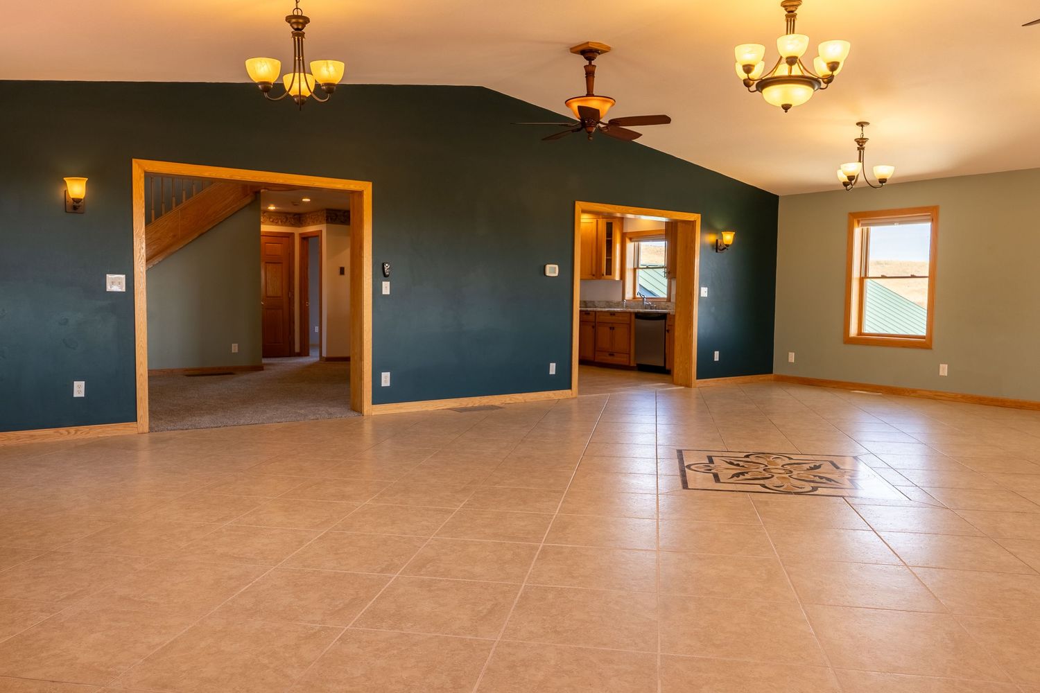 Spacious open-concept living area with teal walls, tile flooring, vaulted ceilings, and elegant chandeliers in a modern home.