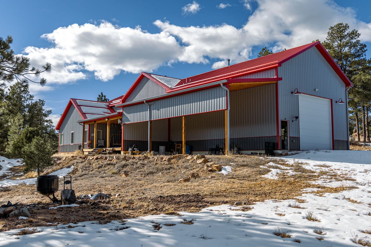 Modern red-roofed barn-style buildings with wooden posts on snowy terrain.