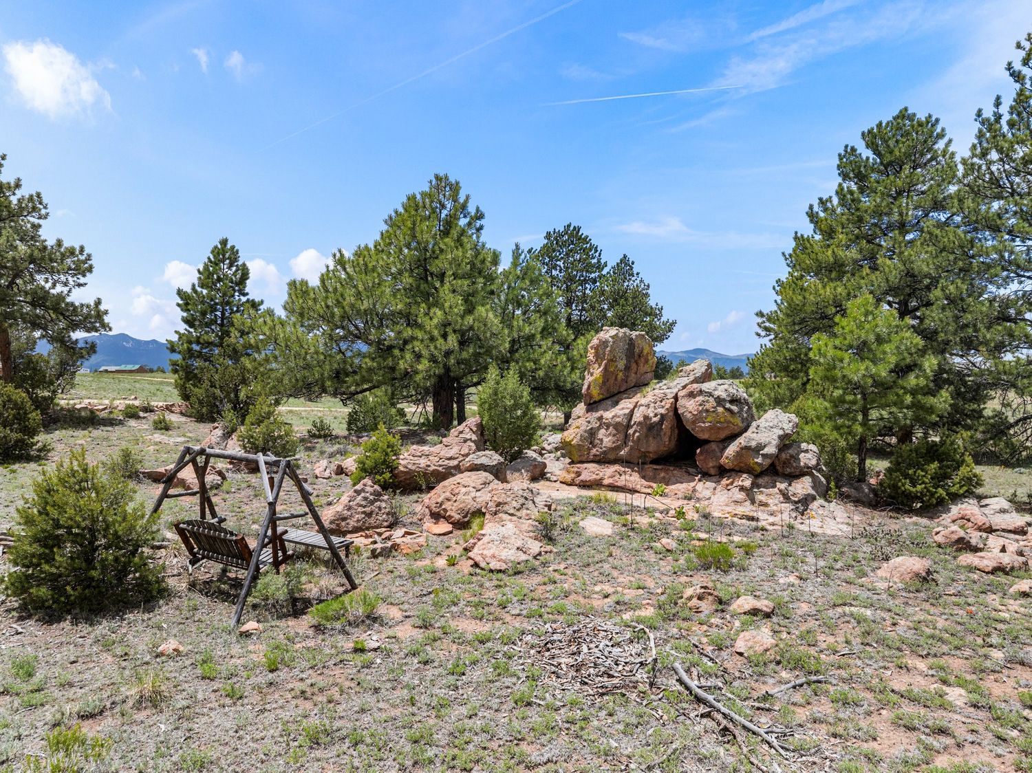 Rocky outcropping with pine trees and vintage wooden swing set on open Colorado mountain property.