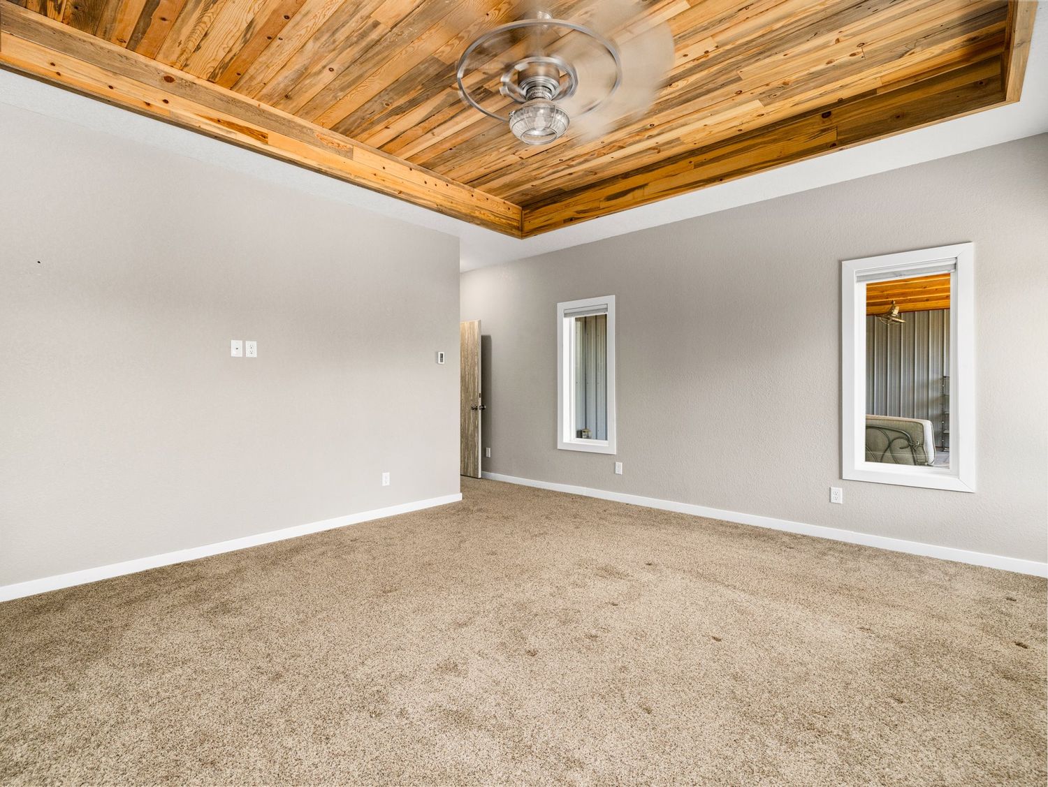 Spacious bedroom with wood plank ceiling, ceiling fan, neutral carpet, and two windows with natural light.
