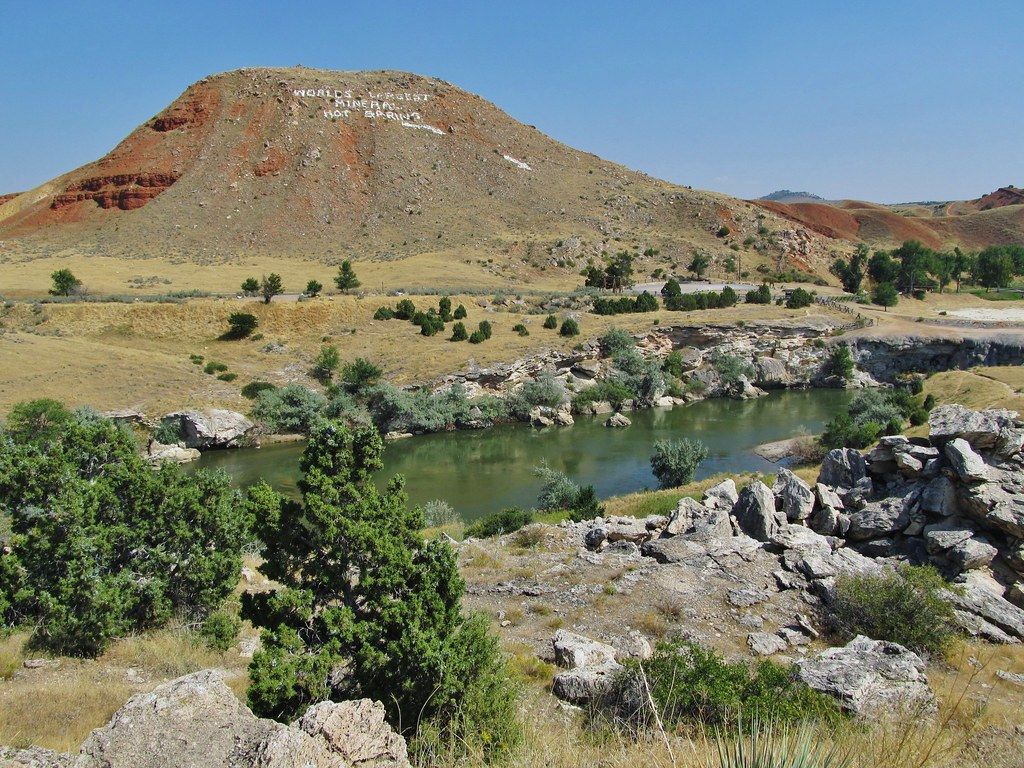 Rocky river winds through arid Wyoming landscape with red and white mesa hill under clear blue summer sky.