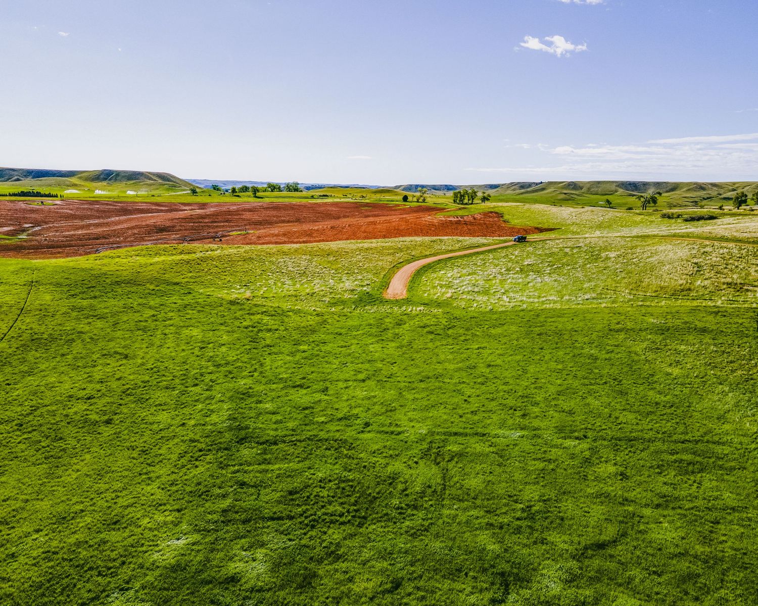 Panoramic view of expansive green meadows with scattered hay bales under blue skies.