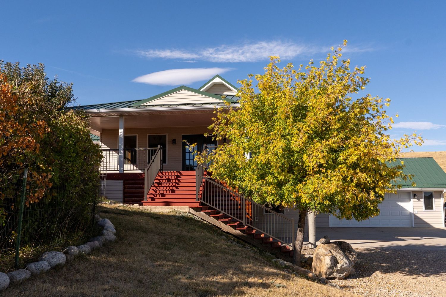Charming two-story home with red staircase and vibrant autumn tree under clear blue sky.