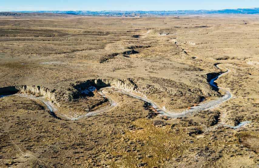 Aerial view of a winding dry riverbed cutting through vast arid plains under a clear blue sky.