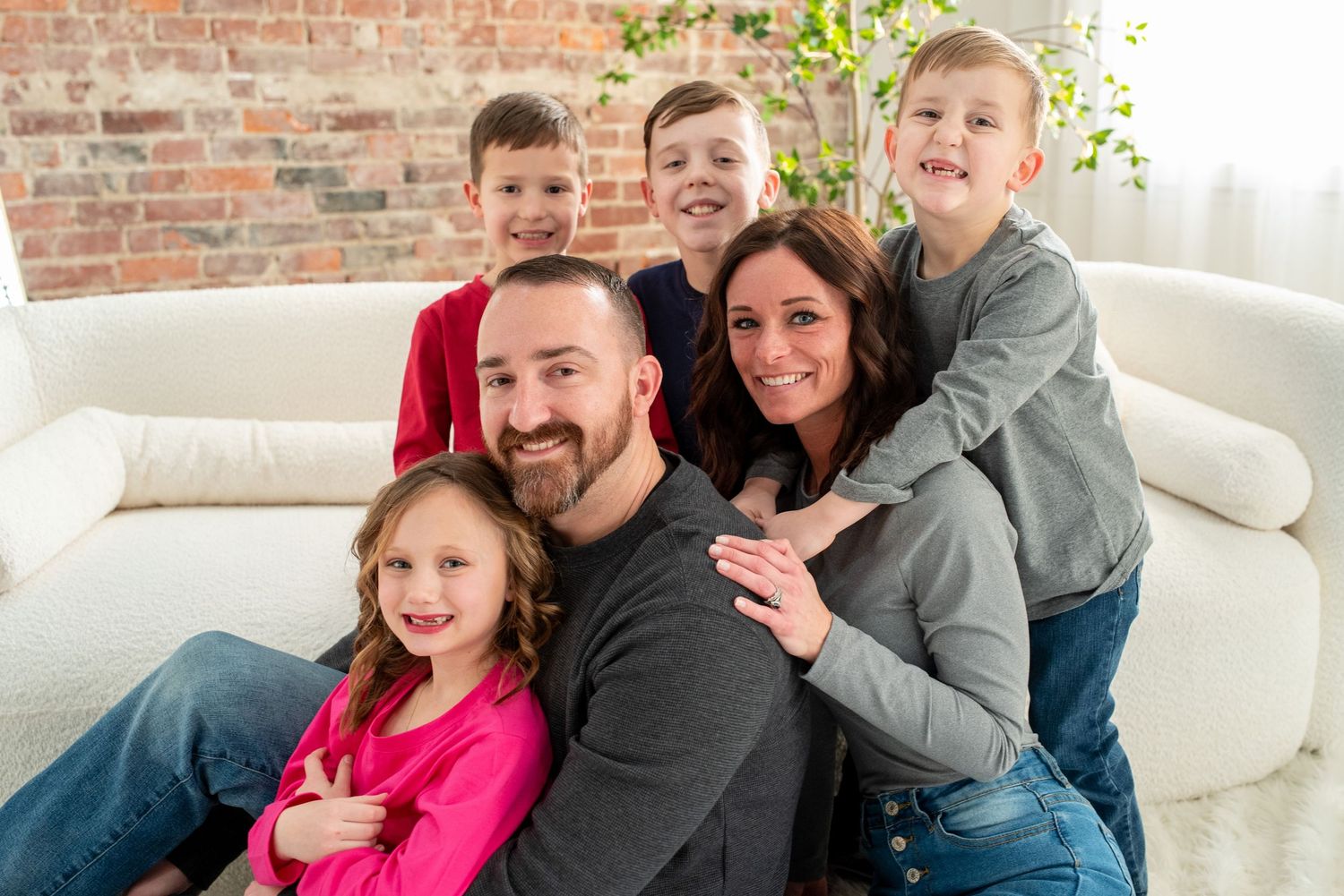 Family members snuggle together on a cozy white couch while sharing laughs and smiles during a casual gathering.