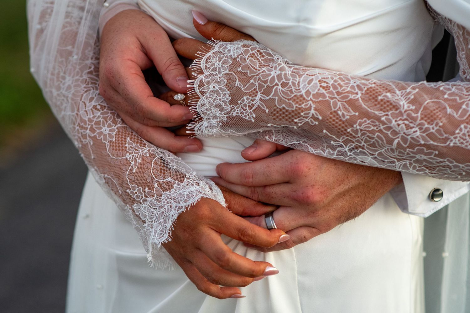 Close-up of delicate lace detail on wedding dress sleeve with hands showing ring.