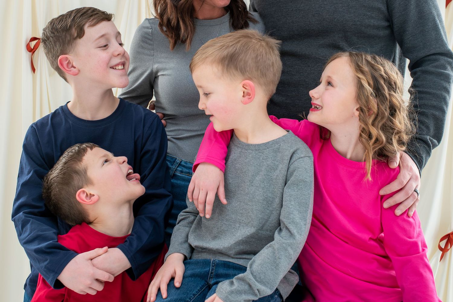 Four siblings share a joyful moment together while laughing and embracing in casual clothing.