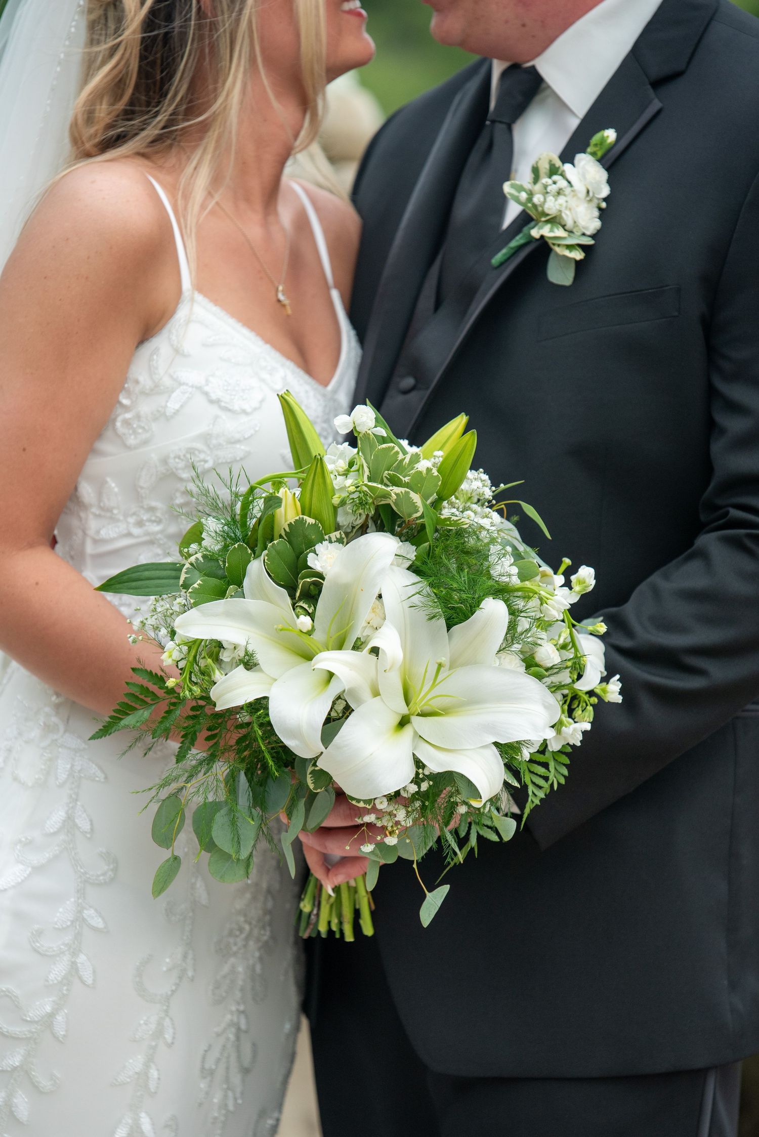Close-up of bride and groom with elegant white floral bouquet outdoors.