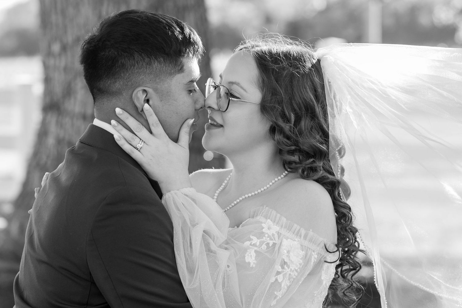 A romantic black and white wedding photo showing couples kissing and embracing under flowing veils.