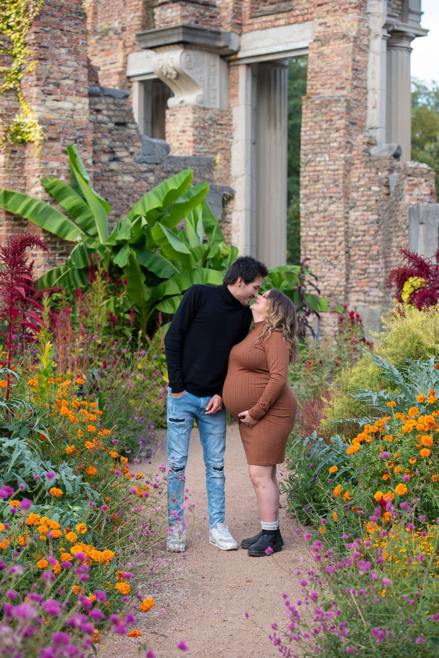 A couple shares an intimate moment in a garden path surrounded by colorful flowers and brick architecture.